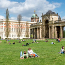 Das Bild zeigt Studierende auf der großen Wiese auf dem Uni-Campus Am Neuen Palais.