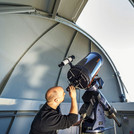 This image shows a scholar who is looking through a telescope in an observatory.