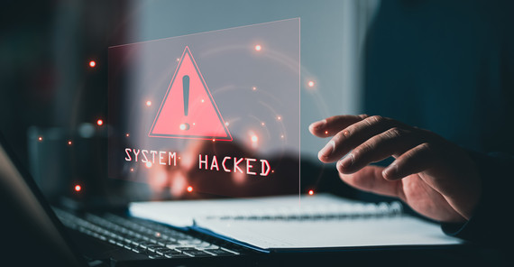 Laptop mit Schriftzug "System hacked" und eine Hand auf der Tastatur