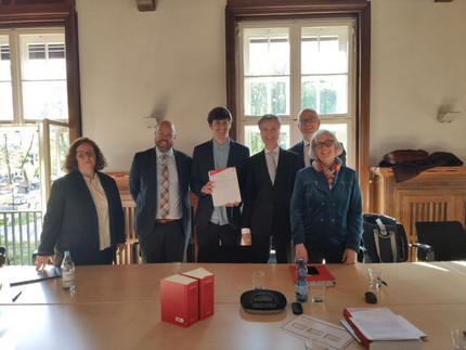 Nach getaner Arbeit 6 Personen stehen hinter einem Tisch, dahinter sind Fenster.