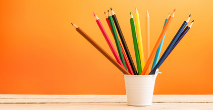 Bunte Stifte in einem Becher vor einem orangen Hintergrund.