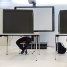 Abbildung zweier Wahlkabinen und einer Wahlurne.