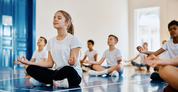 Kinder sitzen in Meditationspose in einer Sporthalle