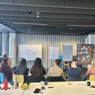 Verschiedene Menschen sitzen in einem Halbkreis vor Moderationswänden und unterhalten sich.