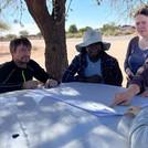NamTip researchers jointly looking at a map opened on the bonnet of a 4x4 car and in the shade of a tree