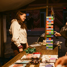 zwei Menschen unterhalten sich an einem Marktstand, daneben ein Jenga Turm