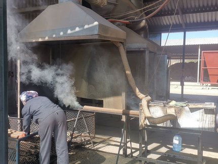 Worker in front of device emitting smoke from burning wood to produce briquettes