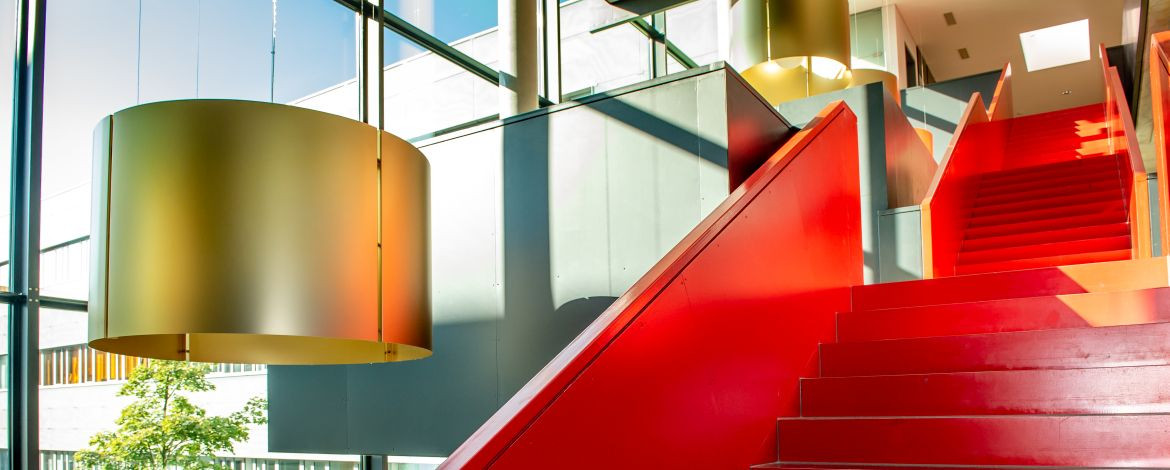 Rote Treppe in einem Foyer mit großem Glasfenster und Blick in den Innenhof