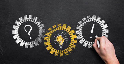 Tafel mit Kreidezeichnungen von Fragezeichen, Glühbirne und Ausrufezeichen