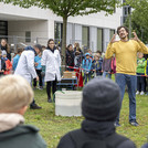 Mann mit gelbem Pullover steht auf einer Wiese und erklärt etwas für eine Gruppe Kinder
