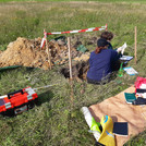 Zwei Personen auf Wiese in gegrabener Grube