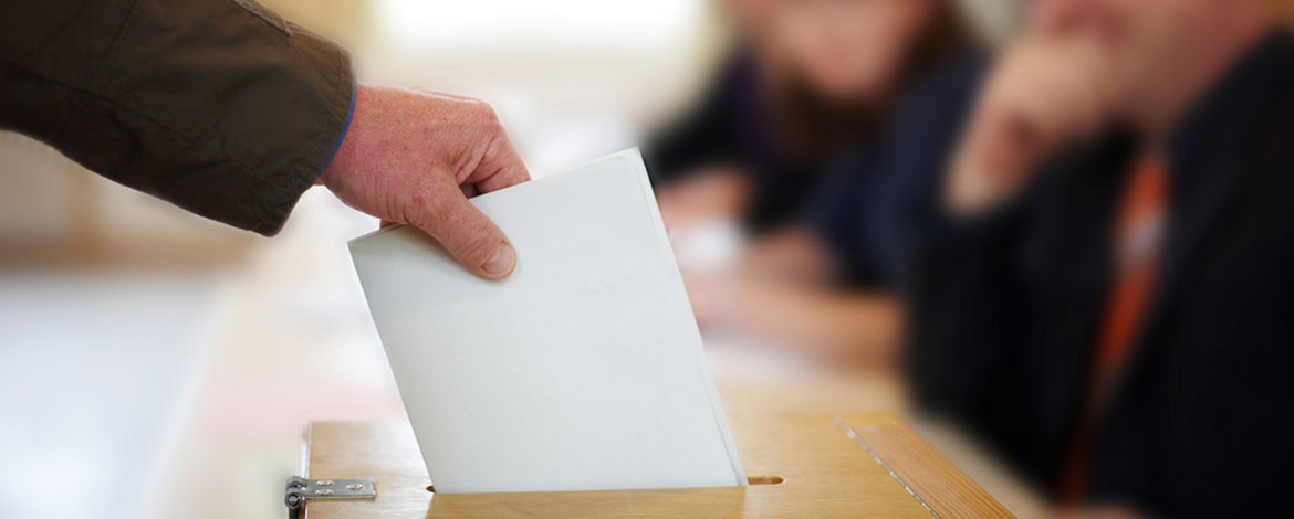 Jemand steckt seinen Stimmzettel in eine Wahlurne - 