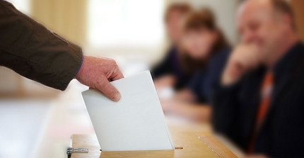 Jemand steckt seinen Stimmzettel in eine Wahlurne