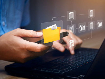 Person at a laptop with an overlay of various pictograms Person sitting at a laptop with a cell phone, typing, with pictograms arranged as an overlay above it