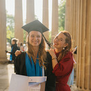 Absolvent*in posiert mit Gast vor den Säulen der Kolonnade.