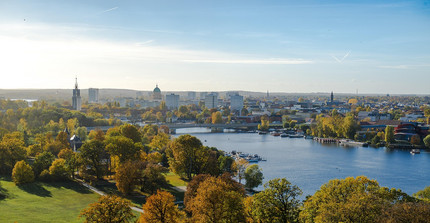 Man sieht die Stadt Potsdam aus der Vogelperspektive. Im Vordergrund sind Bäume sowie die Havel, im Hintergund erhebt sich die Skyline der Stadt.