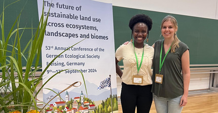 Two researchers standing in front of poster with GfÖ conference title in a classroom