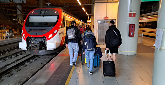 Menschen mit Koffern auf einem Bahnsteig, neben ihnen ein wartender Zug.