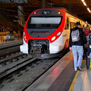 Menschen mit Koffern auf einem Bahnsteig, neben ihnen ein wartender Zug.