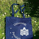 Dunkelblauer Stoffbeutel zentral auf einer grünen Wiese mit weißen Blümchen. Auf dem Stoffbeutel ist das Logo der Universität Potsdam.