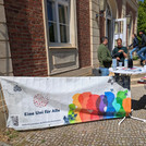Ein Stand vom 5.5. am Neuen Palais mit einem Banner vom Inklusionsteam und Personen die sich unterhalten.