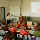 Kinder in einem Klassenraum schauen auf die Dozentin und ein Bild an der Wand