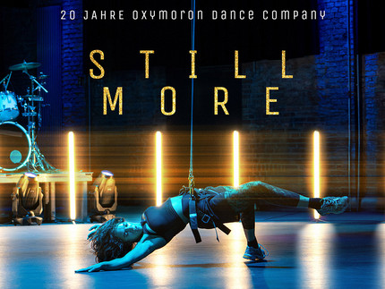 Eine weibliche PErson hängt an einem Seil, das um ihren Bauch festgemacht ist. Im Hintergrund Scheinwerfer und ein Drumset.