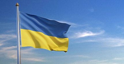 Auf dem Foto ist die wehende urkrainische Flagge zu sehen, im Hintergrund blauer Himmel. Das Foto ist von AdobeStock/Negro Elkha