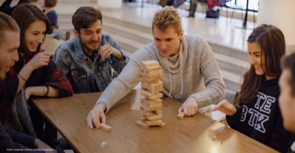 Six young professionals sit around a table and play jenga.