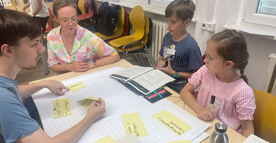 Kinder und Lehrer sitzen um eine Aufgabe.