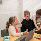 Zwei Erwachsene und drei Kinder arbeiten gemeinsam an Laptops.