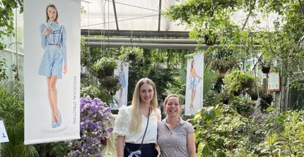 women standing in greenhouse between plants and exhibition posters