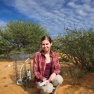 NamTip researcher sitting in front of savanna shrubs with measuring devices, a book and a pen