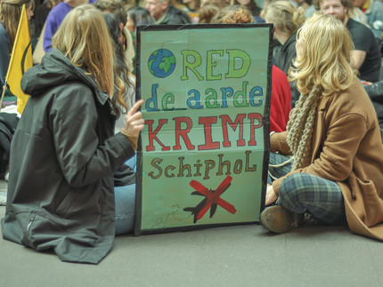 Two women hold a sign that says 'shrink Schiphol'