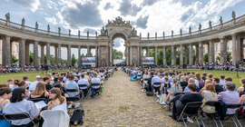 Das Bild zeigt die Gäste, die sich vor der historischen Kulisse der Kolonnade am Neuen Palais versammelt haben.