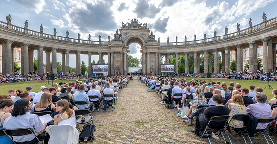 Das Bild zeigt die Gäste, die sich vor der historischen Kulisse der Kolonnade am Neuen Palais versammelt haben.