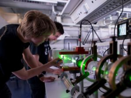 Studierende arbeiten in einem Labor an einem physikalischen Experiment mit einem Laser. Der Laser schießt durch verschiedene optische Apperaturen.
