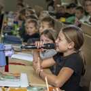 Kind mit Mikrofon in einem Hörsaal voller Kinder