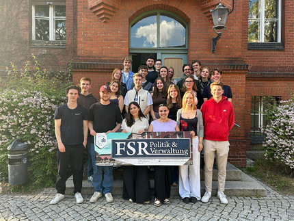 Mehrere Personen stehen vor einem Backsteingebäude, im Vordergrund halten sie ein Banner mit der Aufschrift "FSR Politik und Verwaltung"