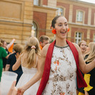 Eine tanzende*r Absolvent*in im Vordergrund. Im Hintergrund tanzen ebenso zahlreiche Menschen.