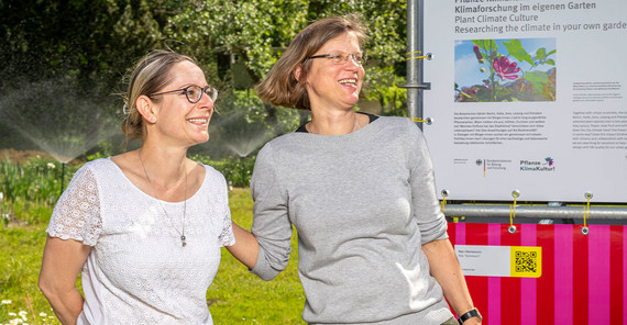 Dorit Siebert (li.) und Prof. Dr. Anja Linstädter vor der Tafel der Ausstellung „Re:Generation“ zum Projekt „Pflanze KlimaKultur!“ im Botanischen Garten der Universität Potsdam.
