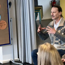 Eine männliche gelesene Person erklärt mit Einsatz seiner Hände anderen Personen etwas im Rahmen eines Workshopsettings.