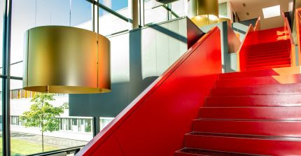 Rote Treppe in einem Foyer mit großem Glasfenster und Blick in den Innenhof