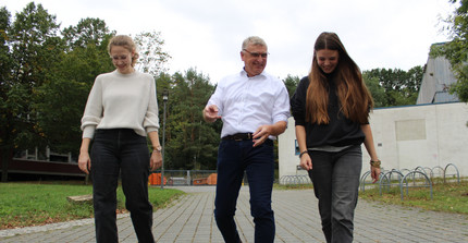 Zu sehen sind drei laufende Personen, zwei Frauen und ein älterer Mann. Sie lachen und reden miteinander.