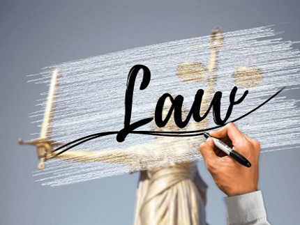 a hand writing the word “Law”; in the background the Justizia