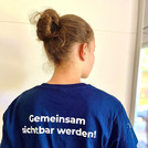 T-Shirt von hinten sichtbar. Darauf steht "Gemeinsam sichtbar werden!".